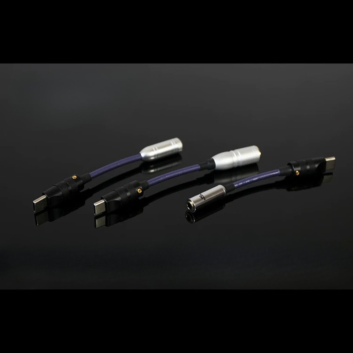 Three USB-C headphone DAC dongles on reflective black surface